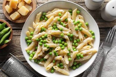 Photo of Delicious pasta with green peas, cheese, grater and fork on wooden table, top view