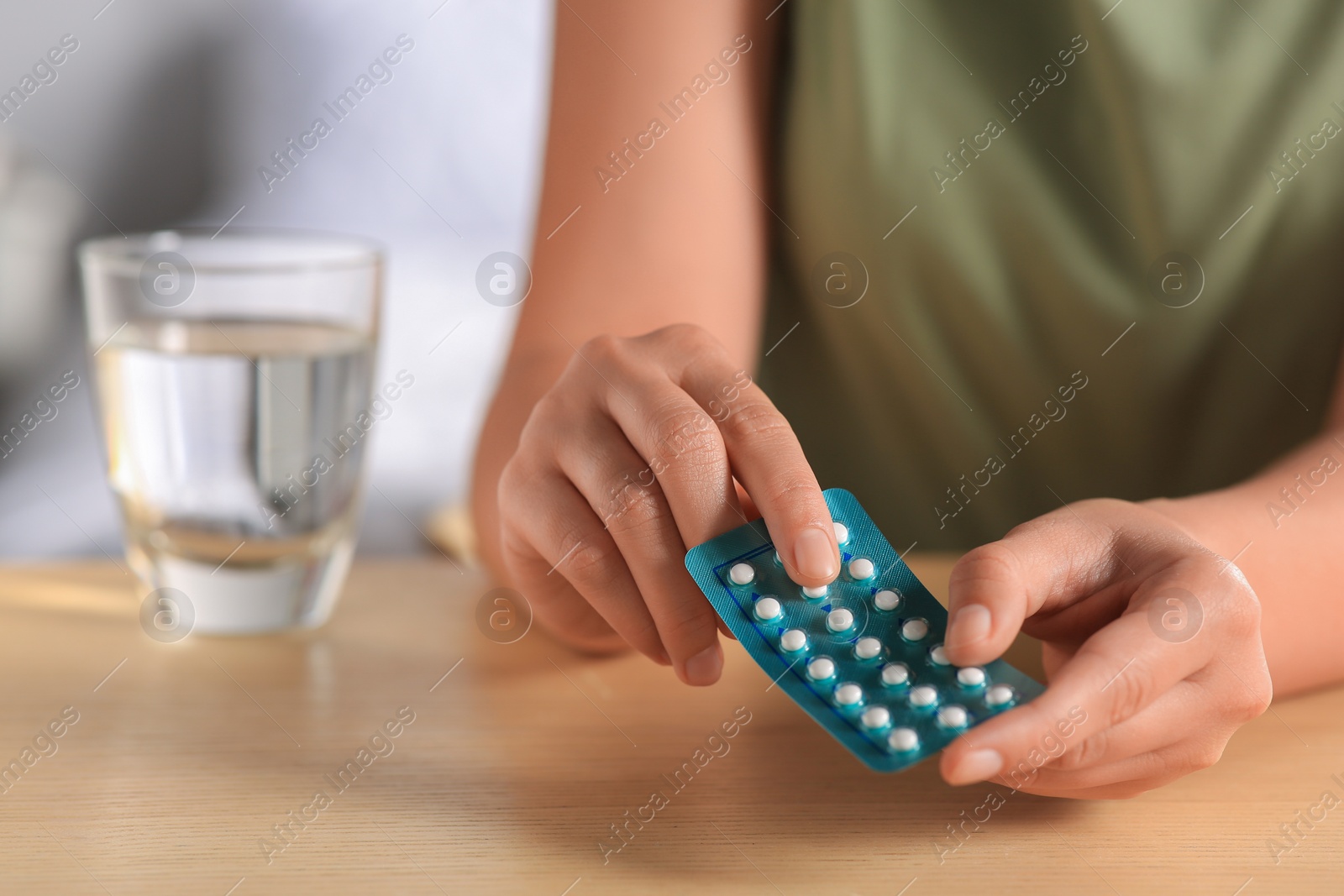 Photo of Woman taking oral contraception pill at wooden table indoors, focus on hands