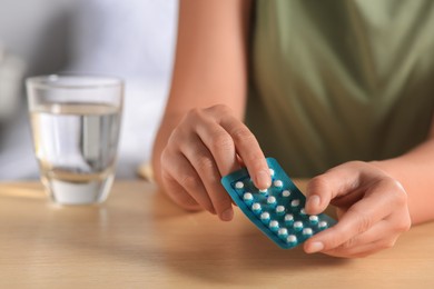 Photo of Woman taking oral contraception pill at wooden table indoors, focus on hands