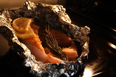 Photo of Foil with fish in oven, closeup. Baking salmon