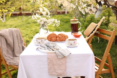 Stylish table setting with beautiful spring flowers, tea and croissants in garden