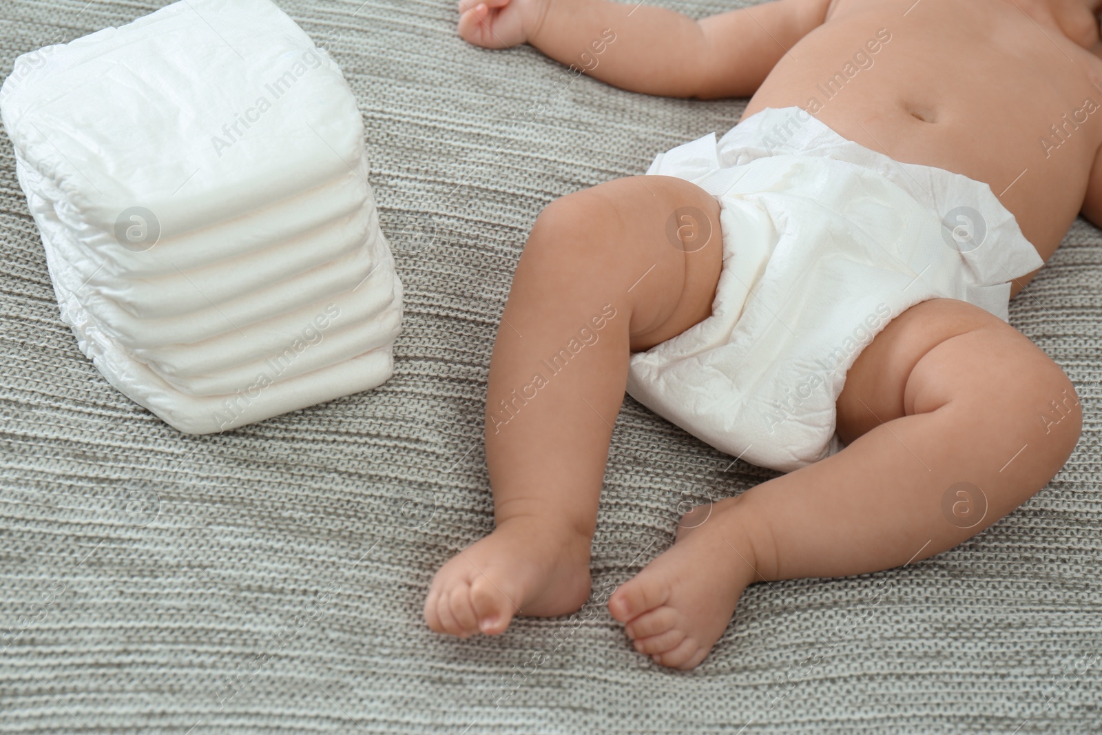 Photo of Cute little baby in diaper on grey blanket, closeup