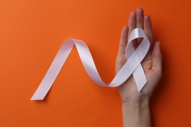Photo of Woman holding white awareness ribbon on orange background, top view