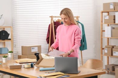 Seller packing bag into cardboard box at table in office. Online store