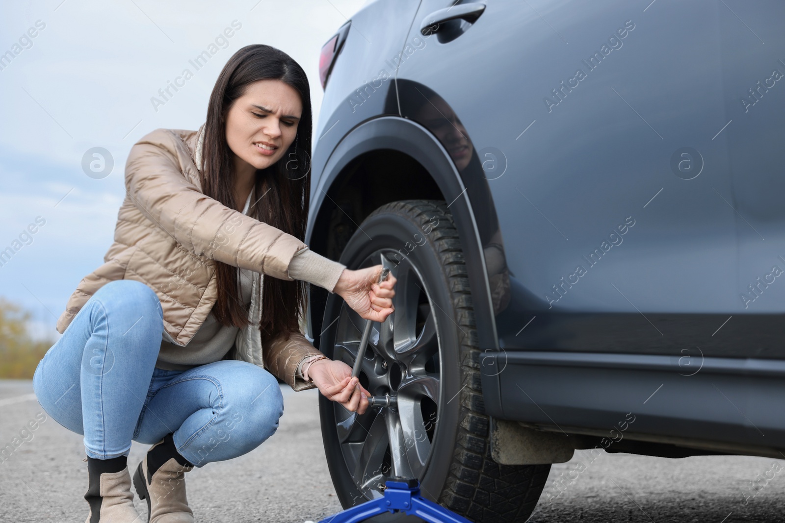 Photo of Worried young woman changing tire of car on roadside