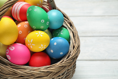 Photo of Colorful Easter eggs in basket on white wooden table, closeup