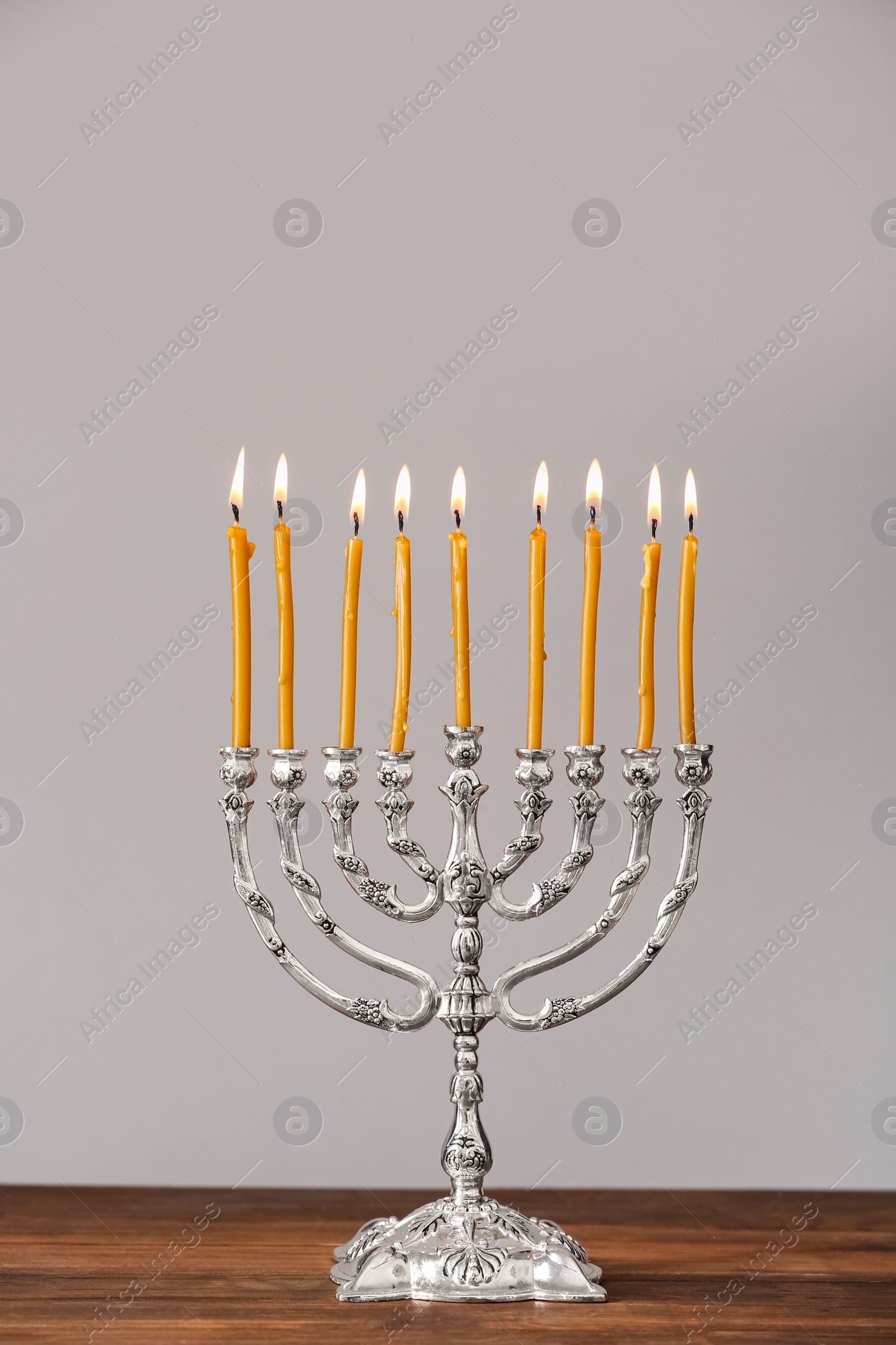 Photo of Silver menorah with burning candles on table against light grey background. Hanukkah celebration