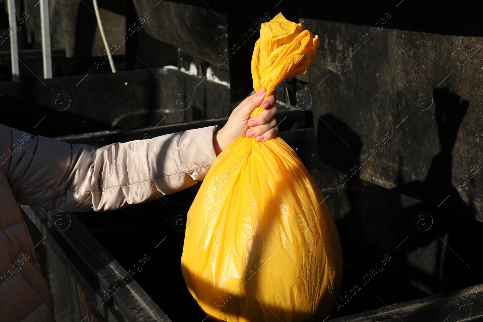 Photo of Woman throwing trash bag full of garbage in bin outdoors, closeup