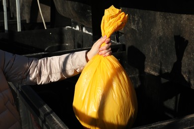 Photo of Woman throwing trash bag full of garbage in bin outdoors, closeup