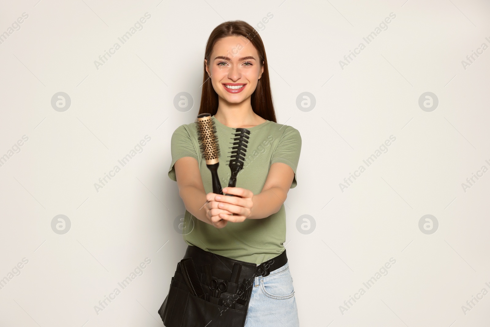 Photo of Portrait of happy hairdresser with brushes on light background