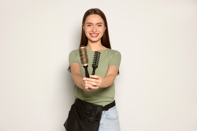 Portrait of happy hairdresser with brushes on light background