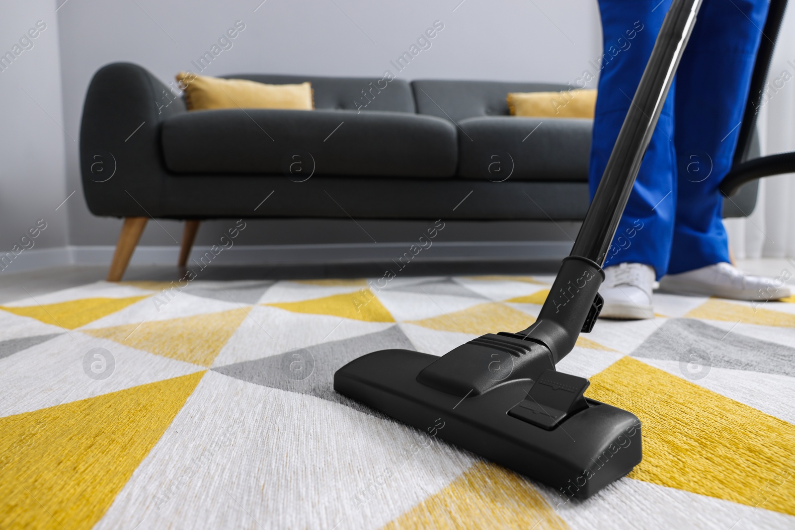 Photo of Dry cleaner's employee hoovering carpet with vacuum cleaner in room, closeup