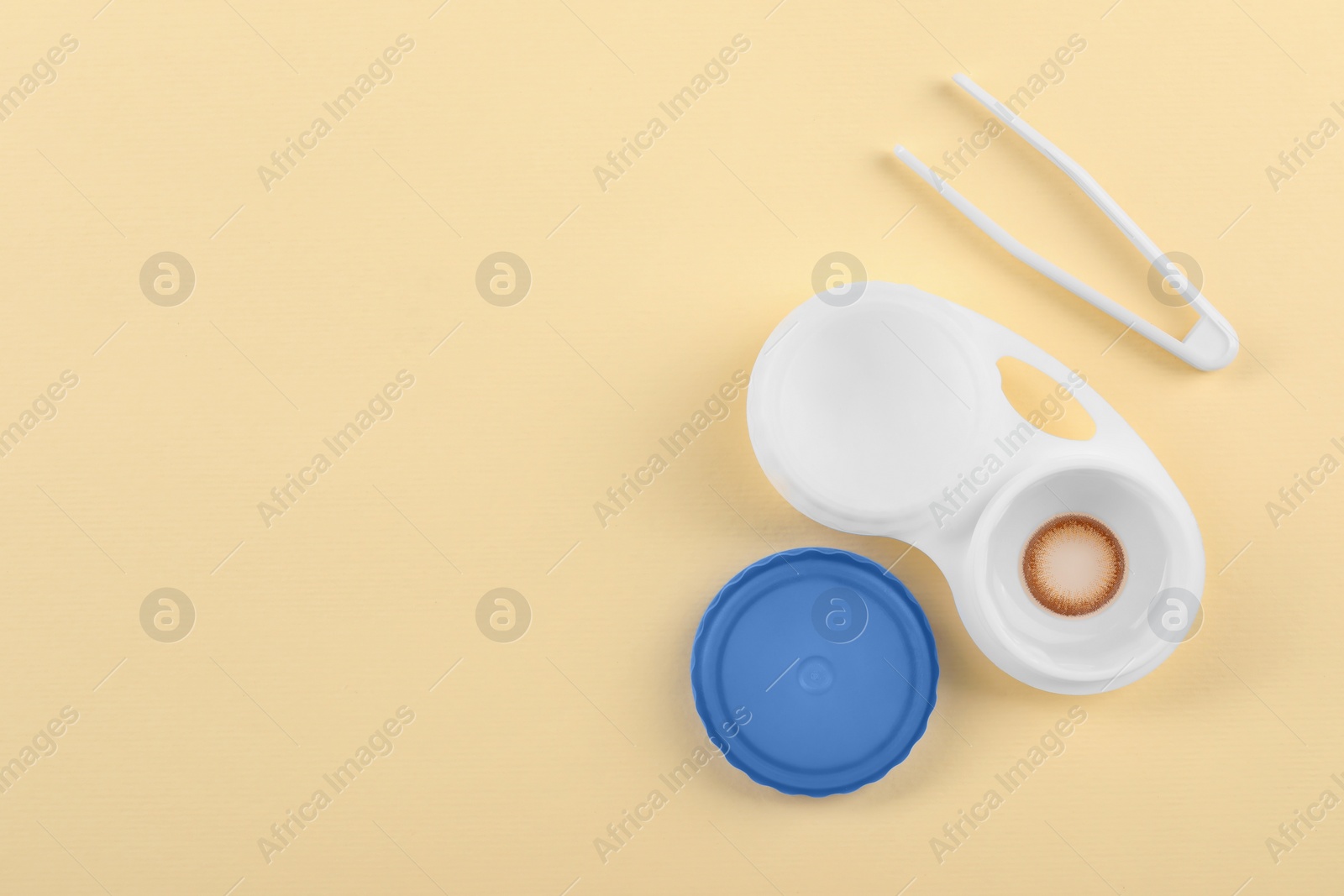 Photo of Case with color contact lenses and tweezers on pale yellow background, flat lay. Space for text