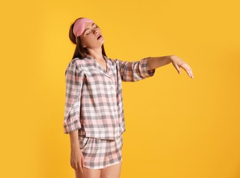 Photo of Young woman wearing pajamas and mask in sleepwalking state on yellow background