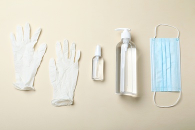 Medical gloves, mask and hand sanitizers on beige background, flat lay