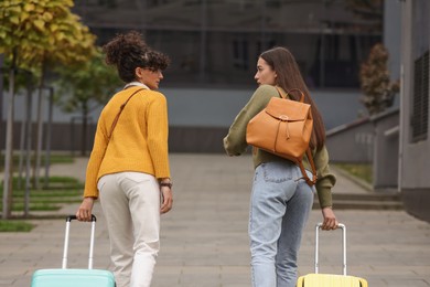 Being late. Worried women with suitcases walking towards building outdoors, back view