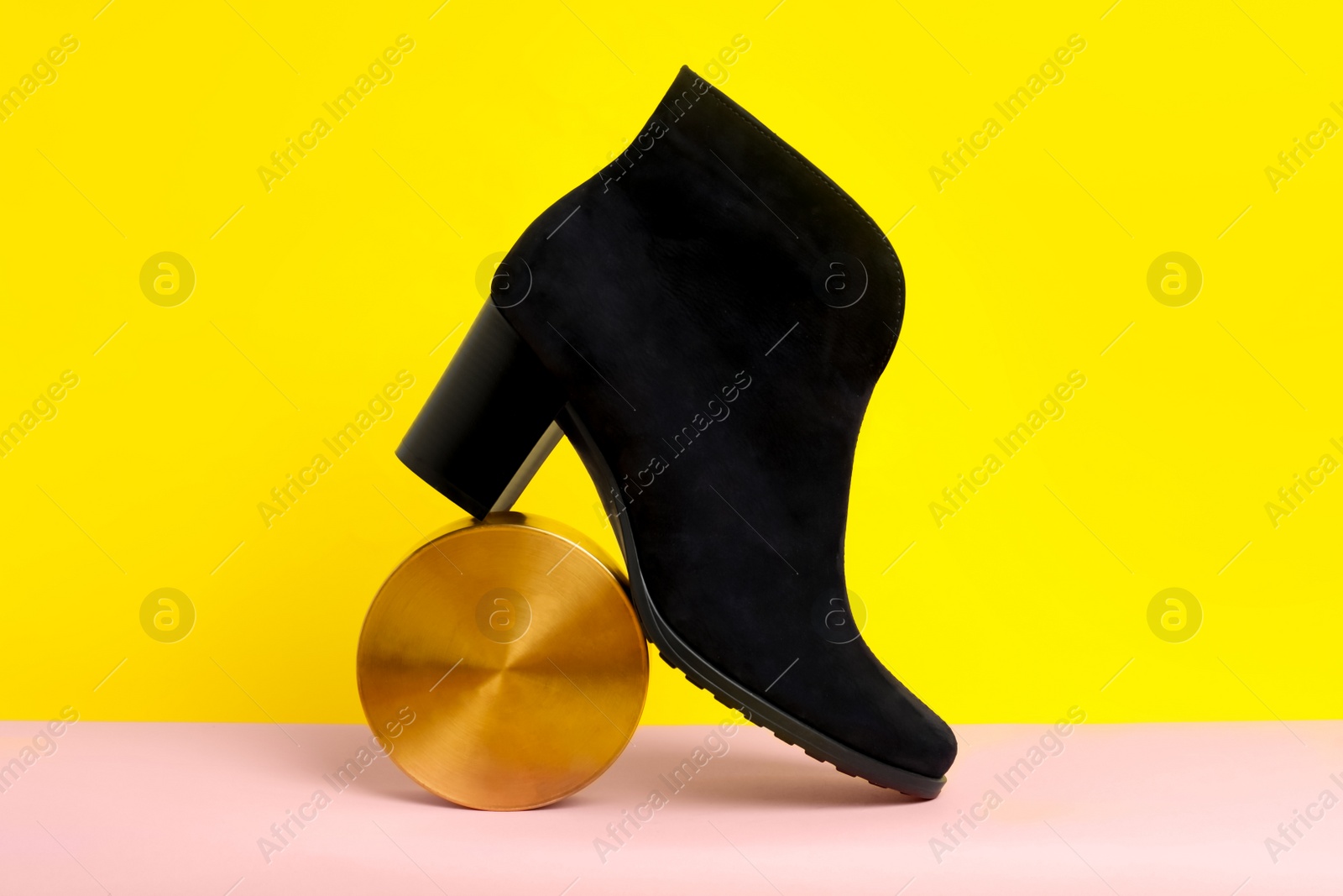 Photo of Stylish black female boot and decor on pink paper against yellow background