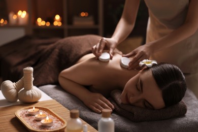 Photo of Spa therapy. Beautiful young woman lying on table during hot stone massage in salon, focus on burning candles