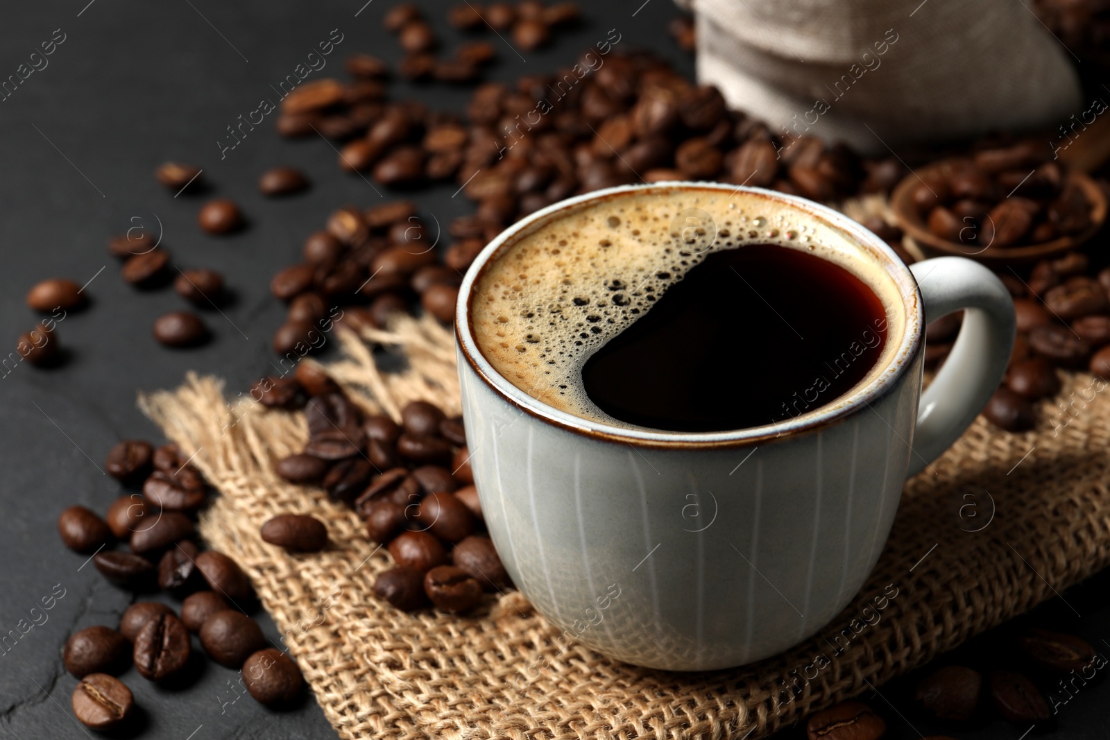 Photo of Cup of aromatic coffee and beans on black table, closeup