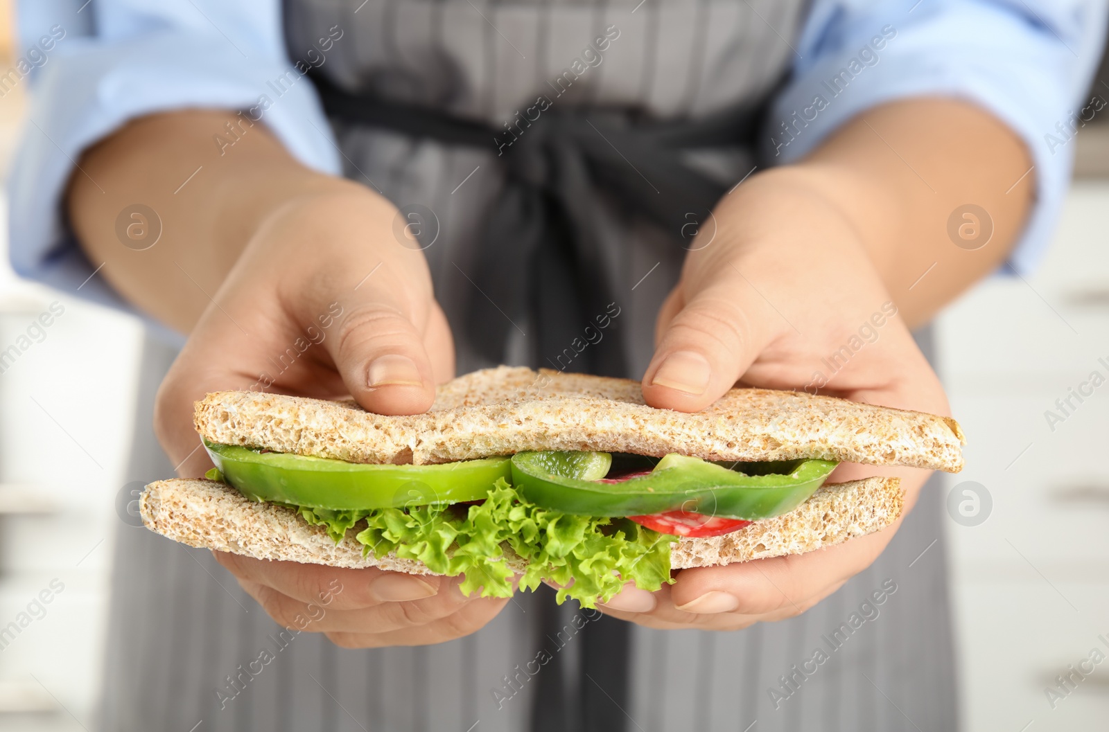 Photo of Woman holding tasty sandwich on light background, closeup