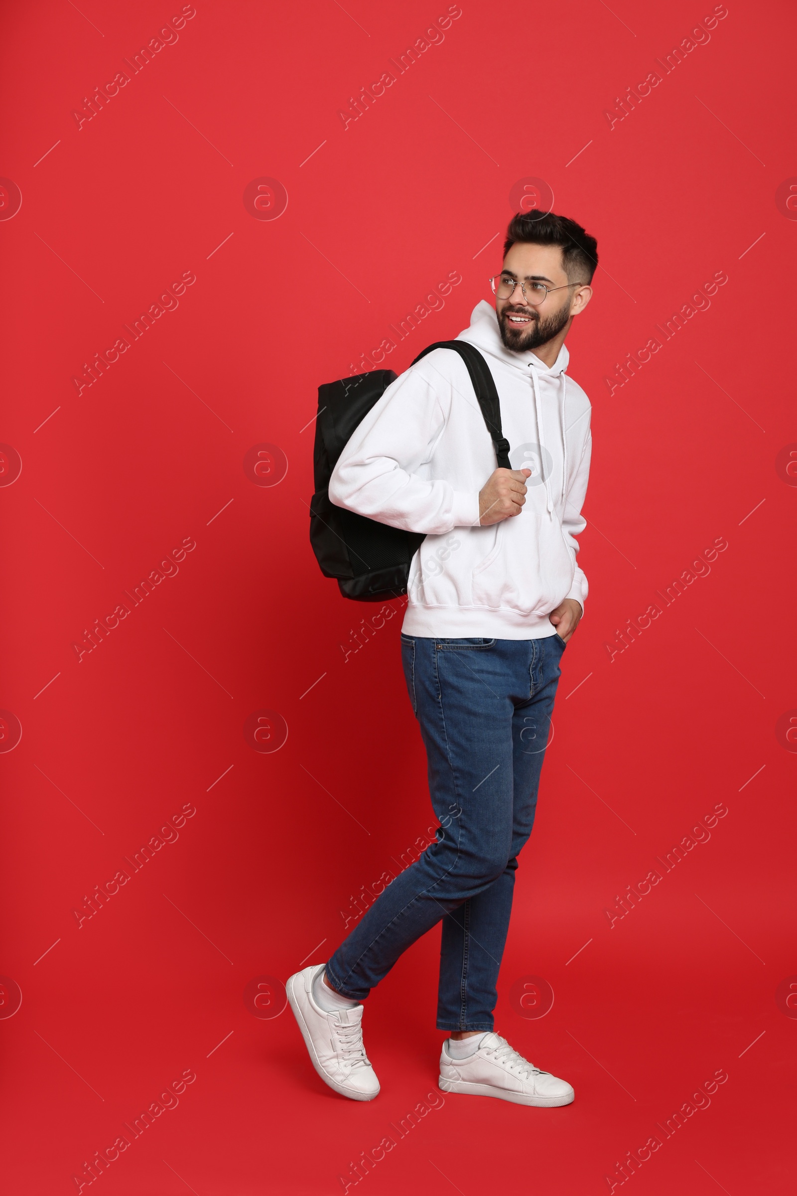 Photo of Young man with stylish backpack walking on red background