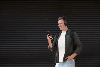 Smiling man in headphones using smartphone near shutters outdoors. Space for text