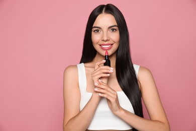 Photo of Young woman with beautiful makeup holding glossy lipstick on pink background