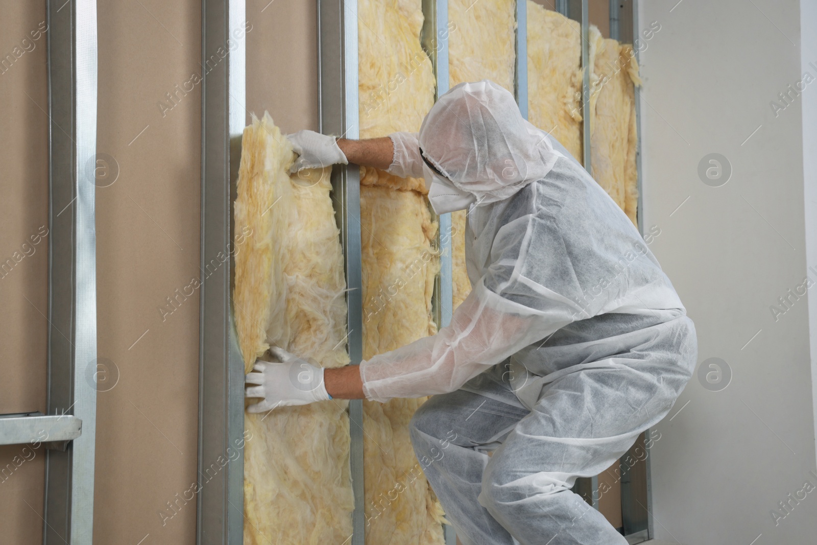 Photo of Worker in uniform and respiratory mask insulating wall indoors