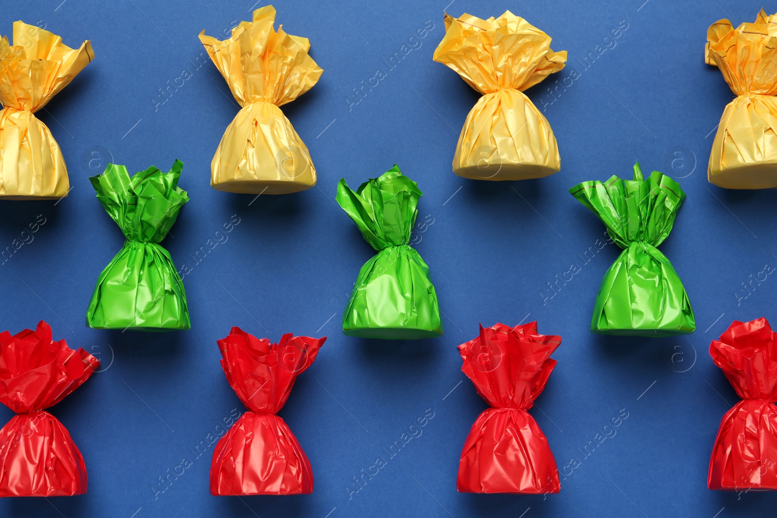 Photo of Many candies in colorful wrappers on blue background, flat lay