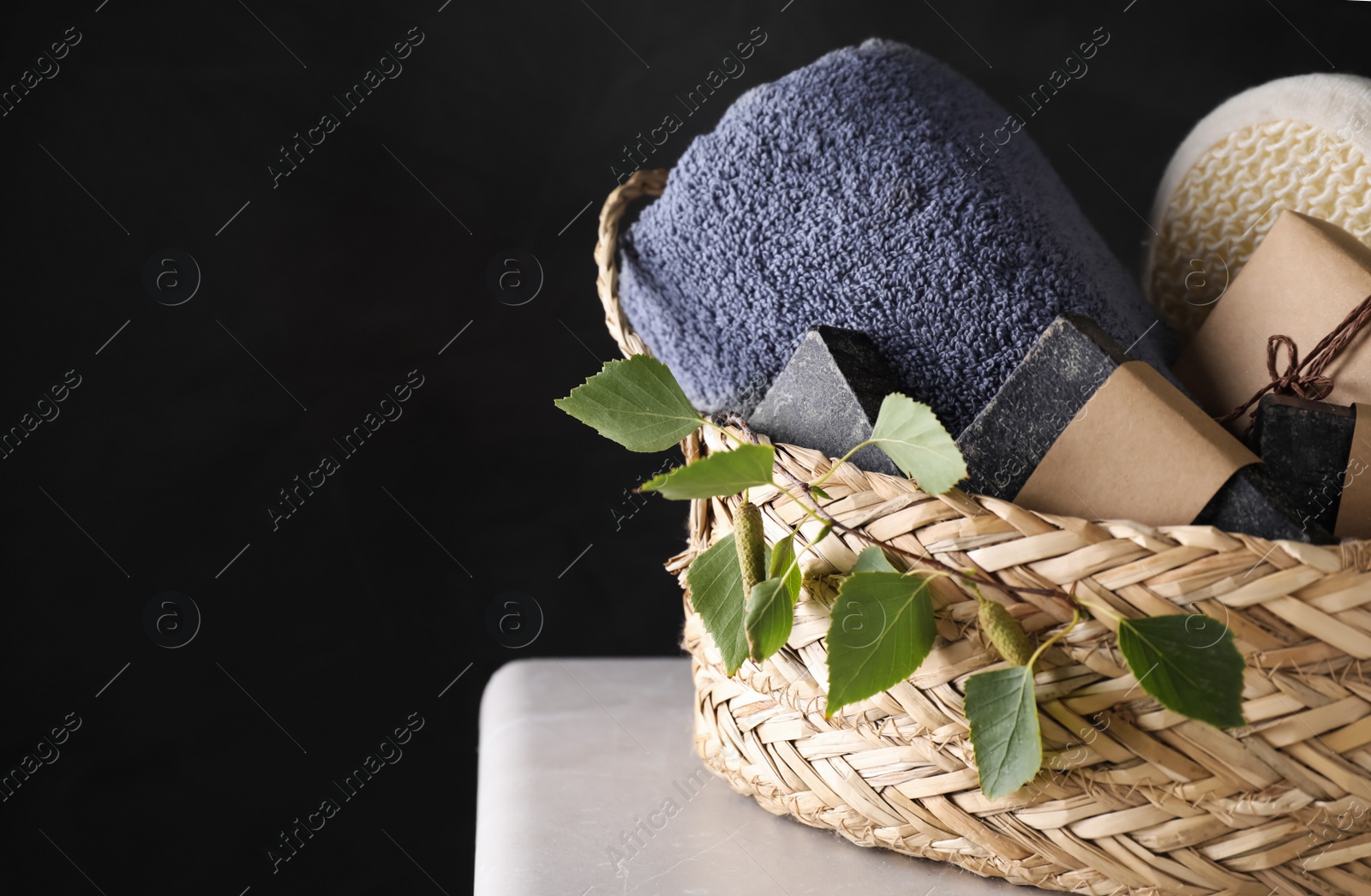 Photo of Natural tar soap in wicker basket on white table against black background. Space for text