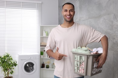 Photo of Happy man with basket full of laundry in bathroom. Space for text
