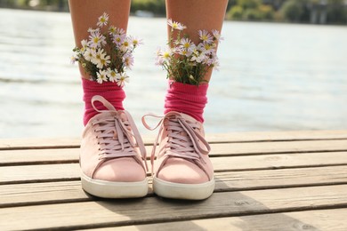 Woman with beautiful tender flowers in socks on wooden pier, closeup