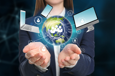 Young businesswoman holding digital image of Earth and different devices in hands on color background, closeup 