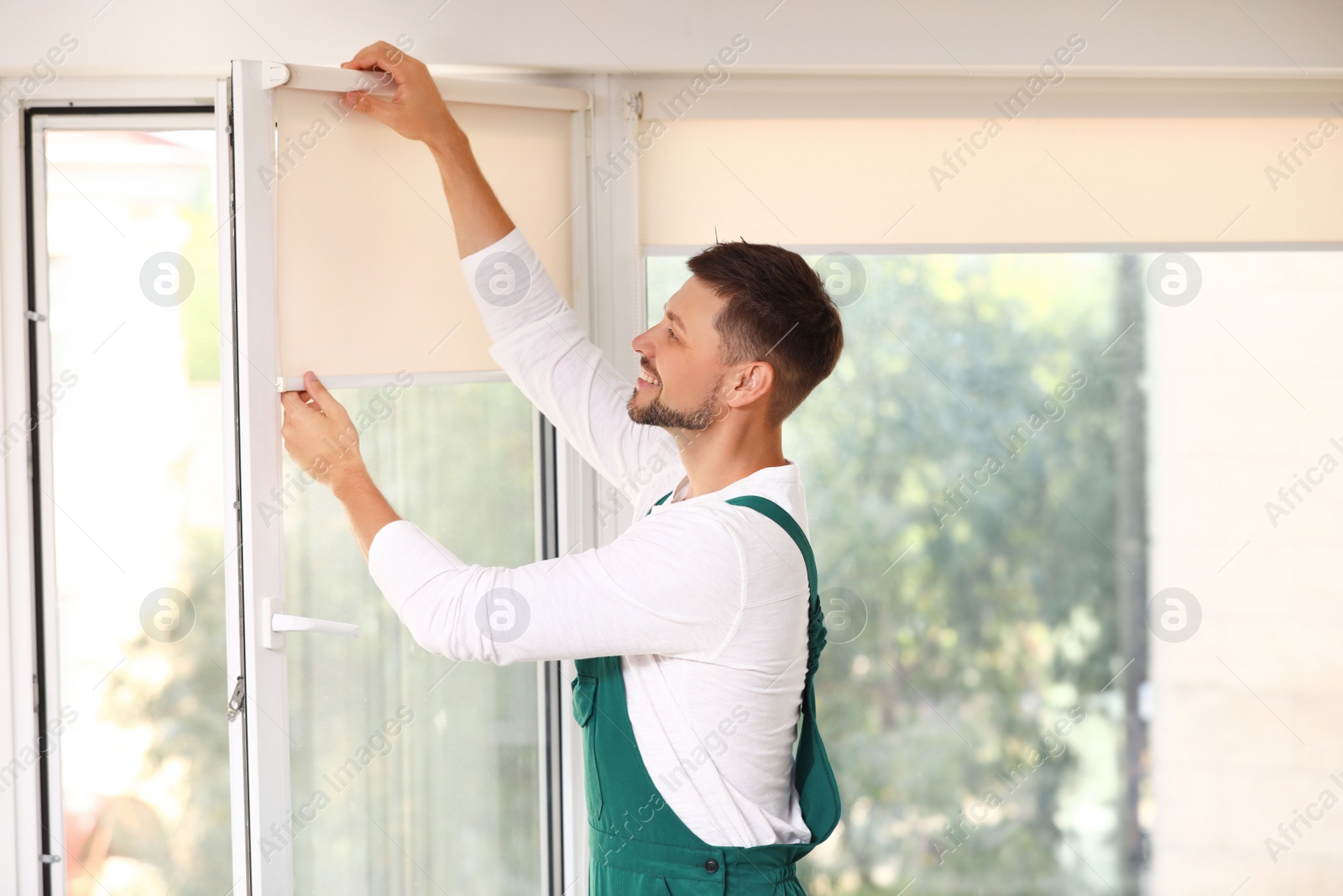 Image of Man in uniform installing roller window blind indoors