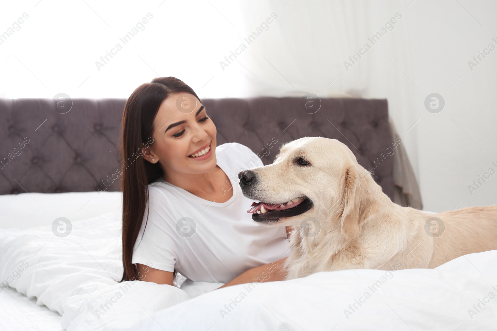 Photo of Young woman and her Golden Retriever dog on bed at home