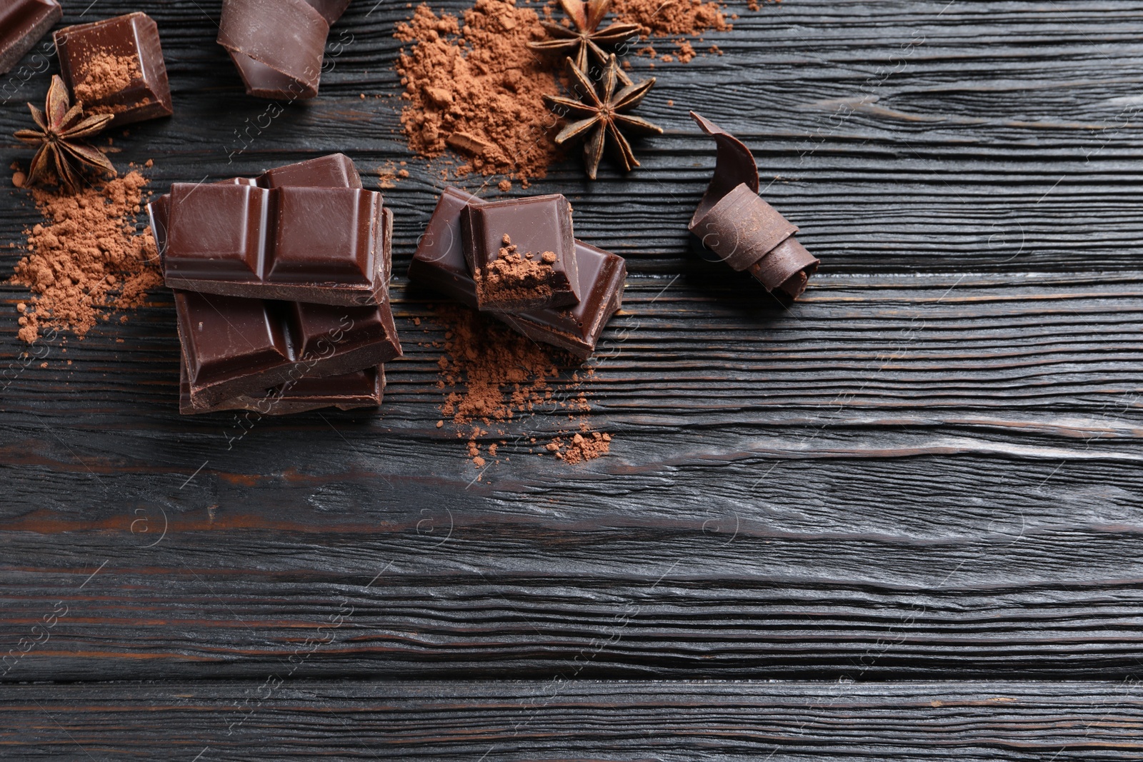 Photo of Pieces of black chocolate on wooden table, flat lay. Space for text