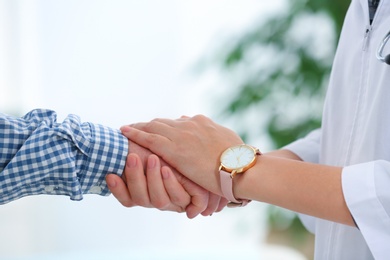 Photo of Doctor holding elderly patient hand on blurred background, closeup