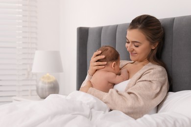 Mother holding her cute newborn baby in bed indoors, space for text