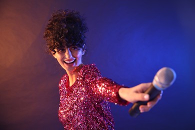 Beautiful young woman with microphone on color background in neon lights