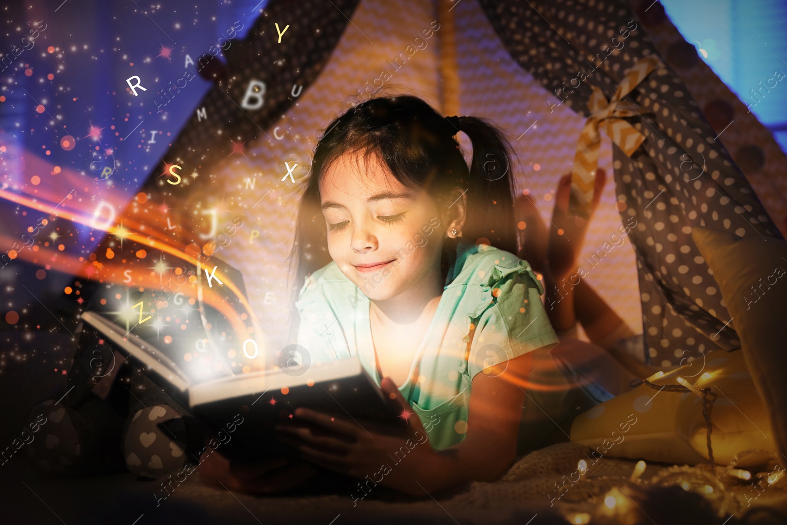 Image of Girl reading shiny magic book with letters flying over it in play tent at home