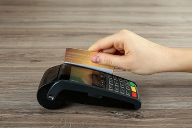 Woman with credit card using modern payment terminal at wooden table, closeup