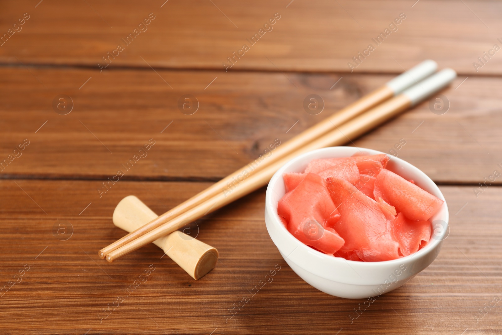 Photo of Pickled ginger in bowl and chopsticks on wooden table, space for text