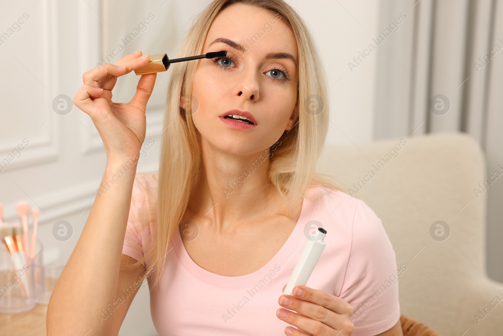 Photo of Beautiful woman applying mascara with brush indoors