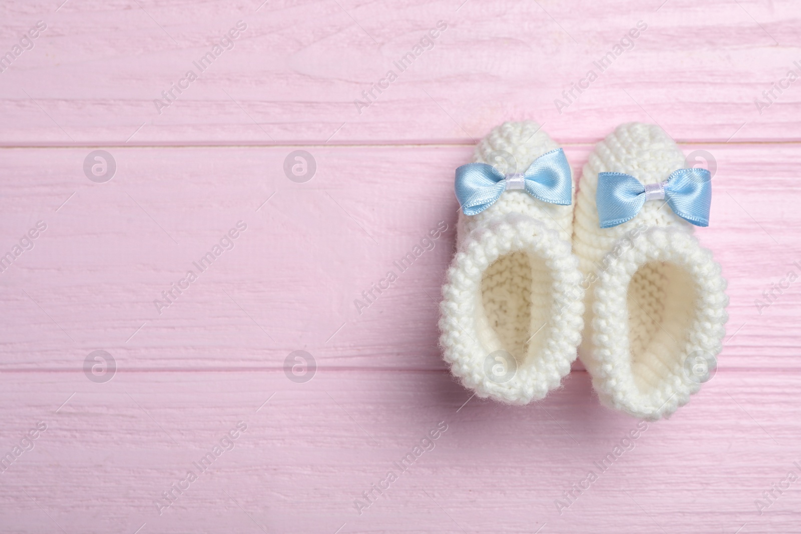 Photo of Top view of child's booties on pink wooden background, space for text