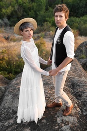 Photo of Happy newlyweds standing on rock outdoors