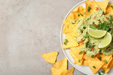 Photo of Plate of delicious mexican nachos chips with guacamole sauce and lime on grey table, flat lay. Space for text