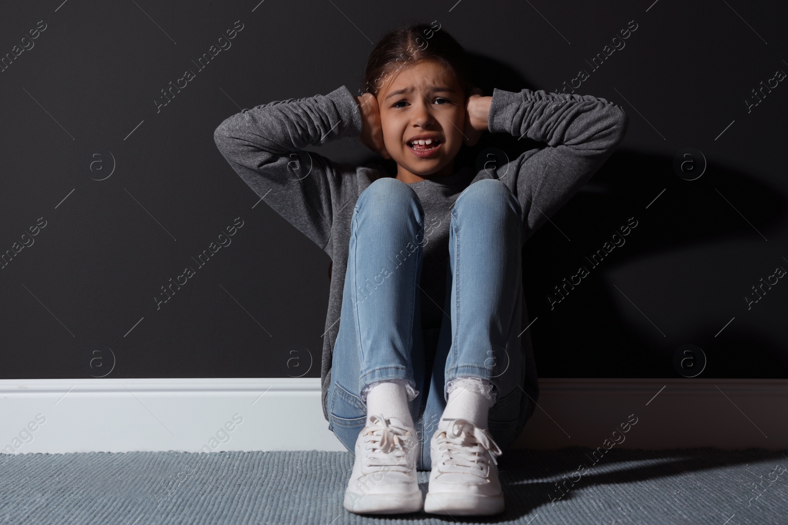 Photo of Scared little girl near black wall. Domestic violence concept