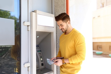 Photo of Young man with money near cash machine outdoors