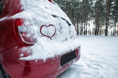 Photo of Heart drawing on snow covered car in winter forest. Space for text