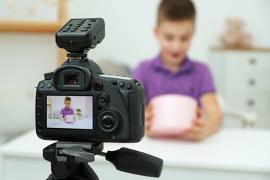 Photo of Emotional little blogger with box recording video at home, focus on camera